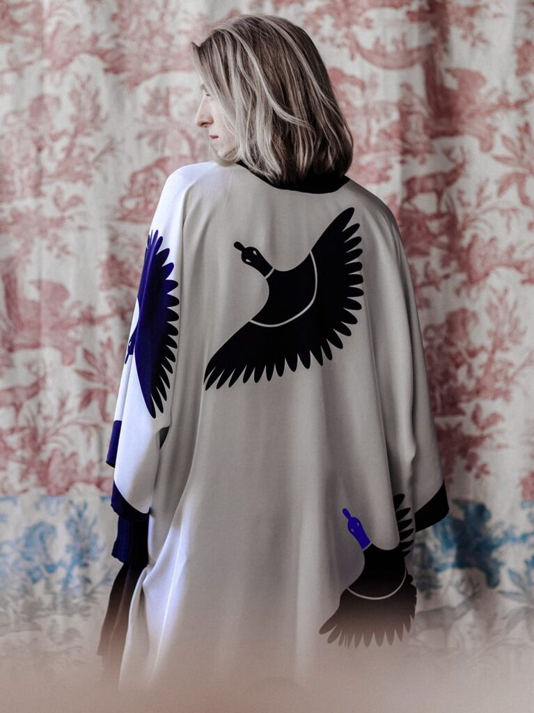 Ansicht einer Frau von hinten mit einem weißen Kimono auf dem eine blaue Sachsenente abgebildet ist.