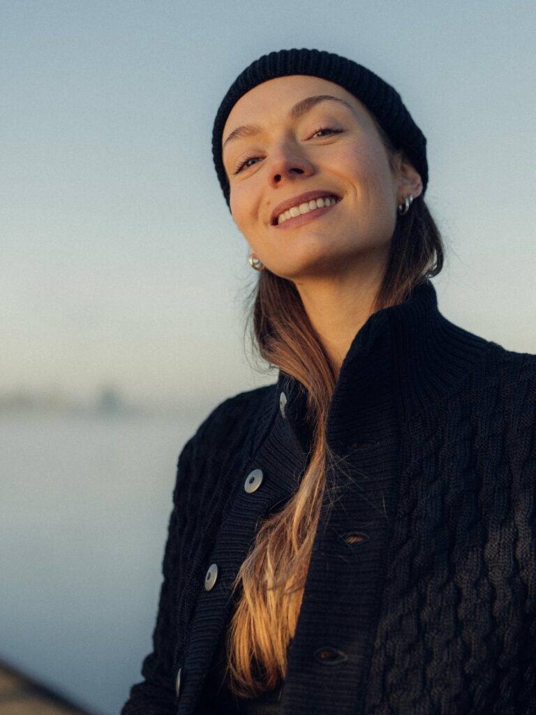 Eine Frau trägt einen H.N.S. Pullover am Ufer. 