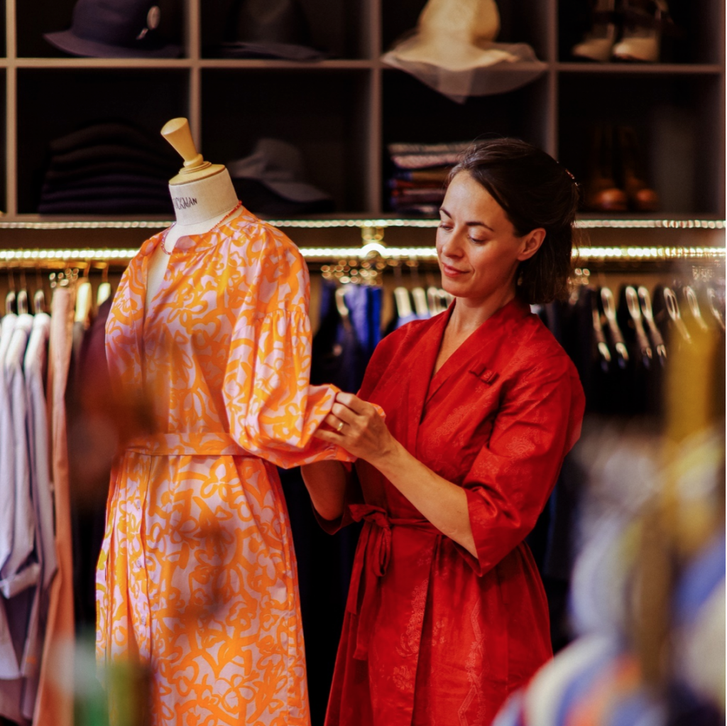 Inhaberin Heike arrangiert ein oranges Kleid auf einer Schneiderpuppe.