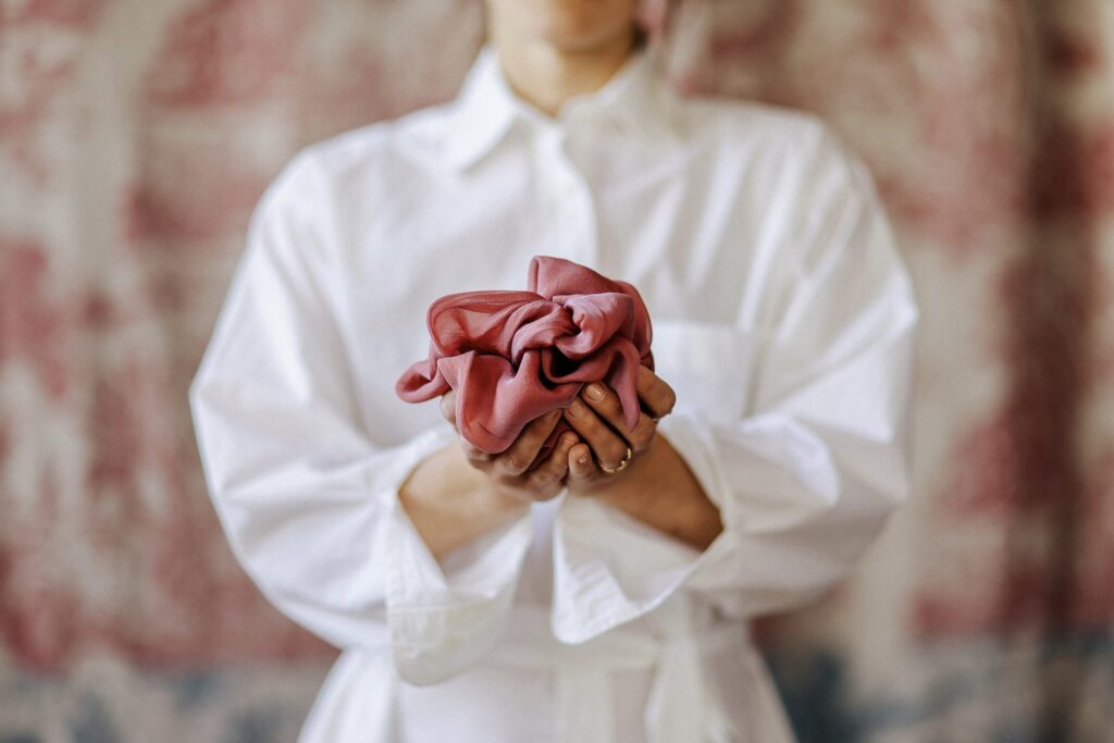 Eine Frau mit weißem Hemd hält ein leicht zusammengedrücktes rosafarbenes Stofftuch.