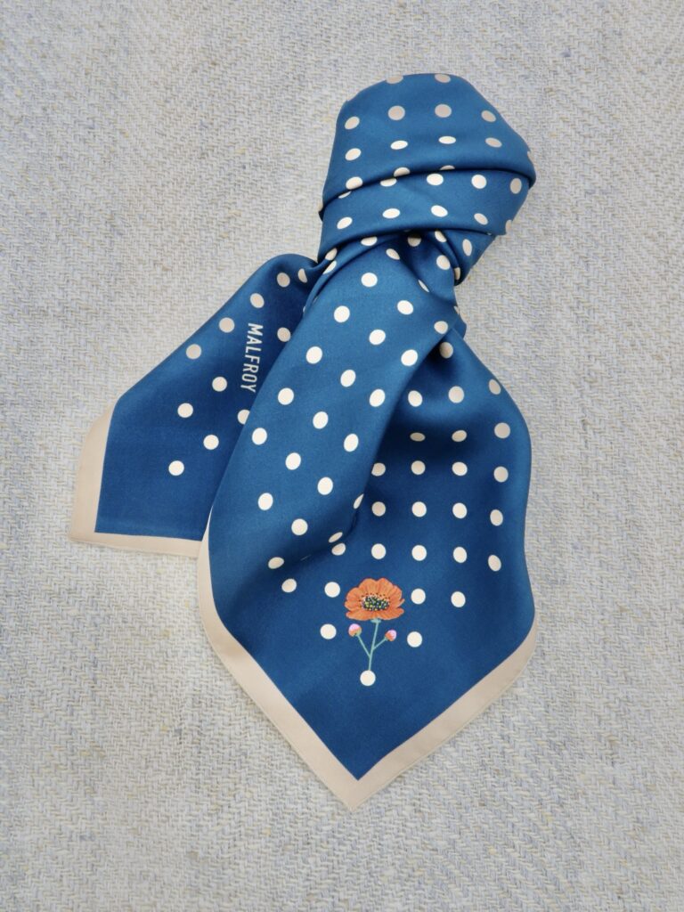 Ein gebundenes blaues Seidentuch mit weißen Punkten und einer Rose von Malfroy